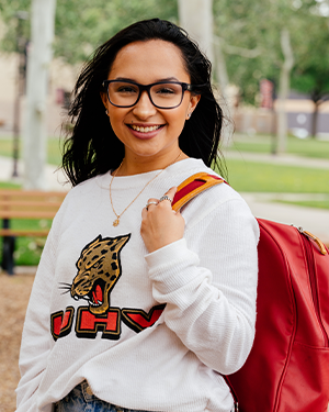 Person in UHV Jaguar sweater with red backpack on campus