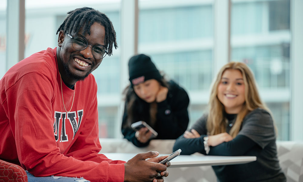Person in a red 'UHV' shirt holding a smartphone, with two others in the background.