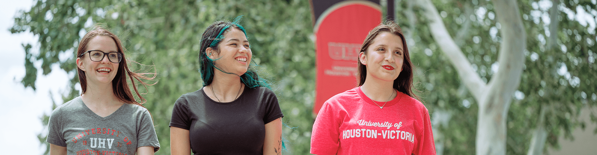 A group of students outdoors on campus near a UHV banner, wearing gray, black, and red shirts with UHV text