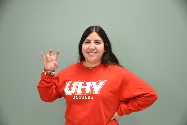 A female wearing red long sleeve UHV Jaguars shirt and doing the UHV Hand Sign.