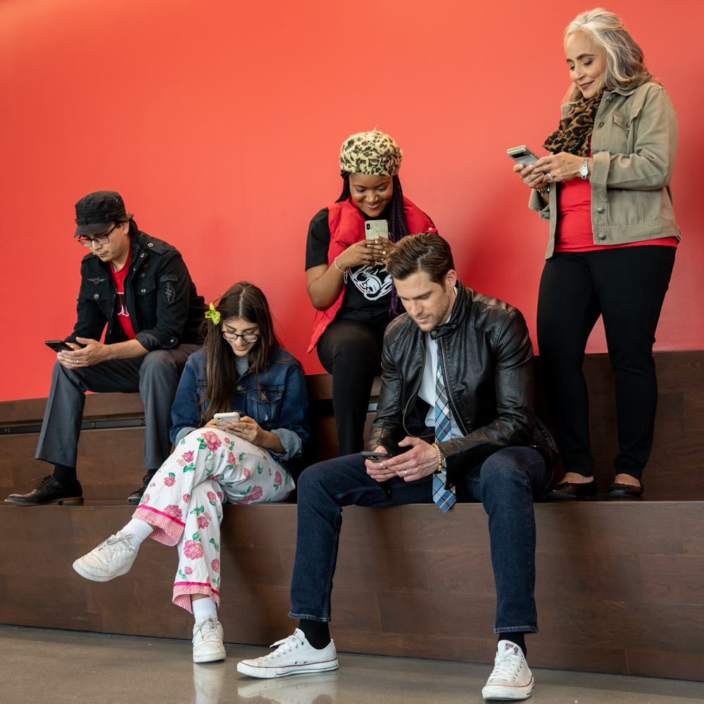 UHV faculty and students staring at their phones in front of a red wall