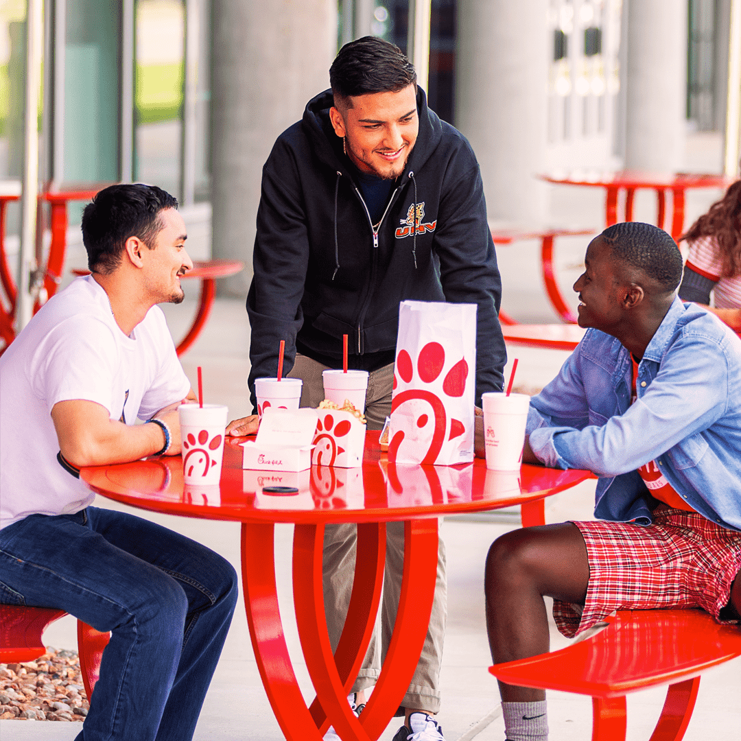 Students sitting at a table outside University Commons, eating Chick-fil-A.