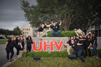 SGA senators posing on the UHV sign at the main entrance to the university.