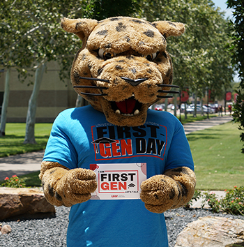 Jax, the UHV mascot, wears a First Gen Day t-shirt and holds a door placard used by First Gen staff members