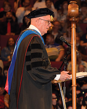 President Bob Glenn in academic regalia speaking at podium during commencement ceremony