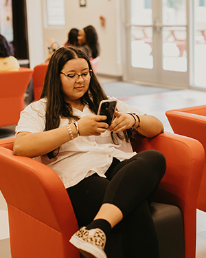 Person sitting on orange chair holding smartphone