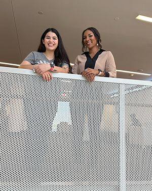 Two people behind metal railing looking down in indoor setting