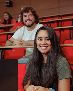 Two people seated in red lecture hall chairs, one in green shirt