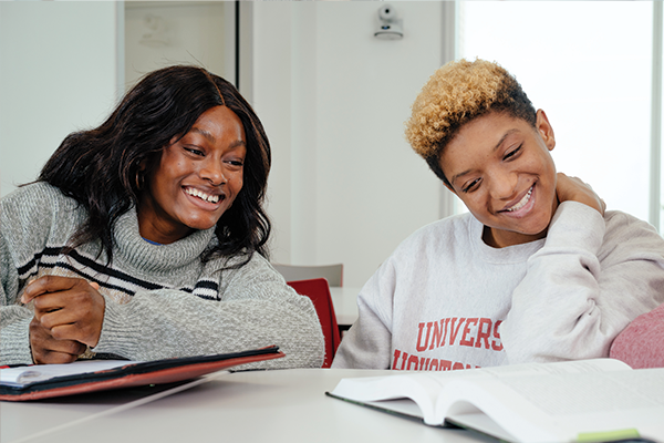 Two female students, smiling while studying.