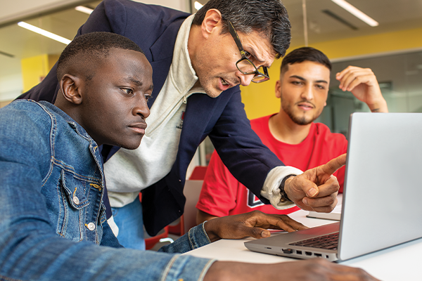 An instructor pointing to a laptop, explaining content to students.