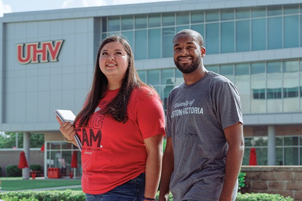 Two students wearing UHV shirts, walking outside University Commons.