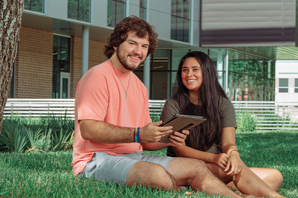 Two students sitting on the grass, outside University South.