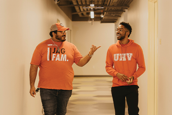 Two individuals walking down a hallway wearing orange shirts with 'JAG FAM' and 'UHV' printed on them.