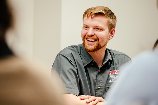 UHV staff member wearing a gray shirt with the UHV logo, sitting at a table and smiling.