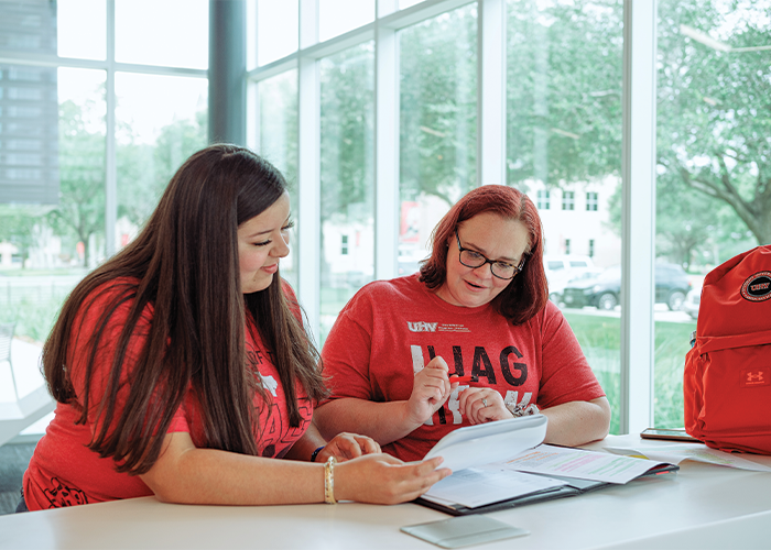Two people in red UHV shirts reviewing papers at table with red backpack