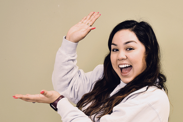 Person with long hair in a light sweatshirt holding hands up as if framing or presenting something