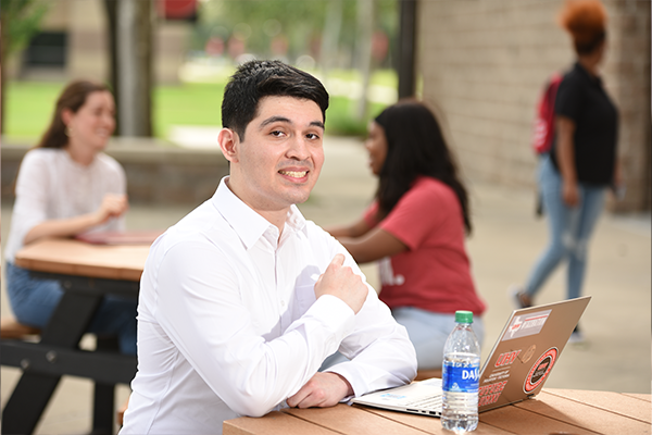 A male student sitting outside with a laptop.