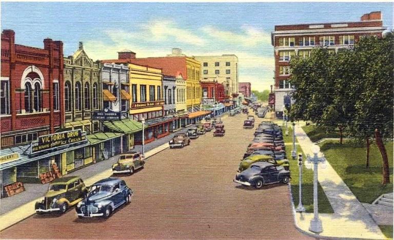 Historic 1940s linen-textured postcard illustrating Main Street, Victoria, Texas, featuring vintage cars and storefronts