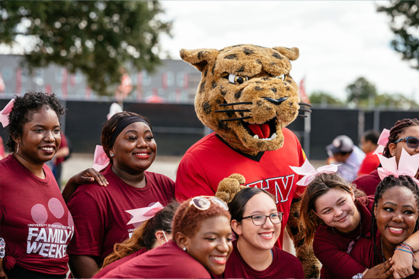 A group of students wearing “UHV Family Weekend” shirts posing outdoors with jaX the jaguar mascot.
