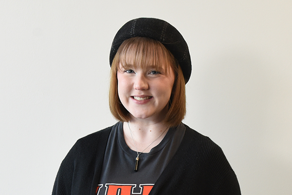A student wearing a black beret, black cardigan, and a dark grey t-shirt with red and white text that includes “UHV,” standing against a plain background.