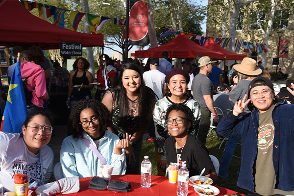 A group of students gathered around a red table at the UHV International Festival with red tents and colorful flags.