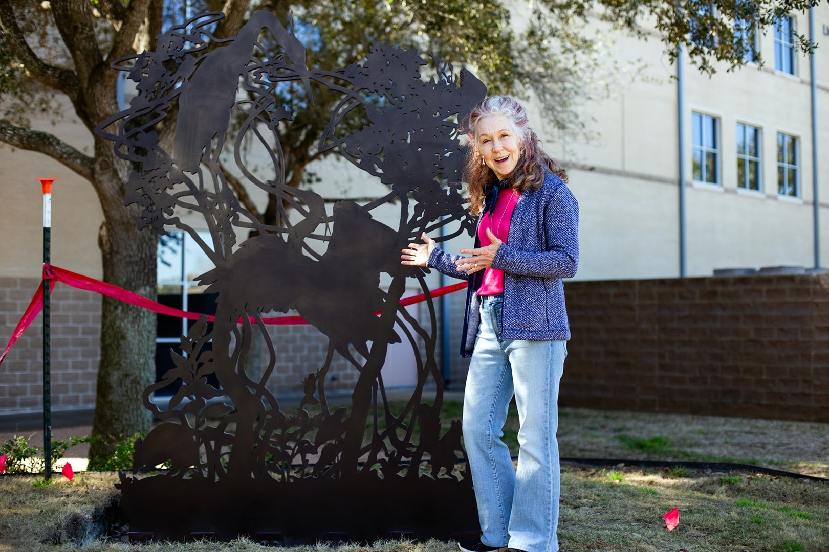 Artist Melissa Miller of Austin stands beside her bronze sculpture, 'Wild Grapes and Herons,' featuring wild grape vines, local flora, fauna, and herons. Installed at Kay’s Grove, February 2024.