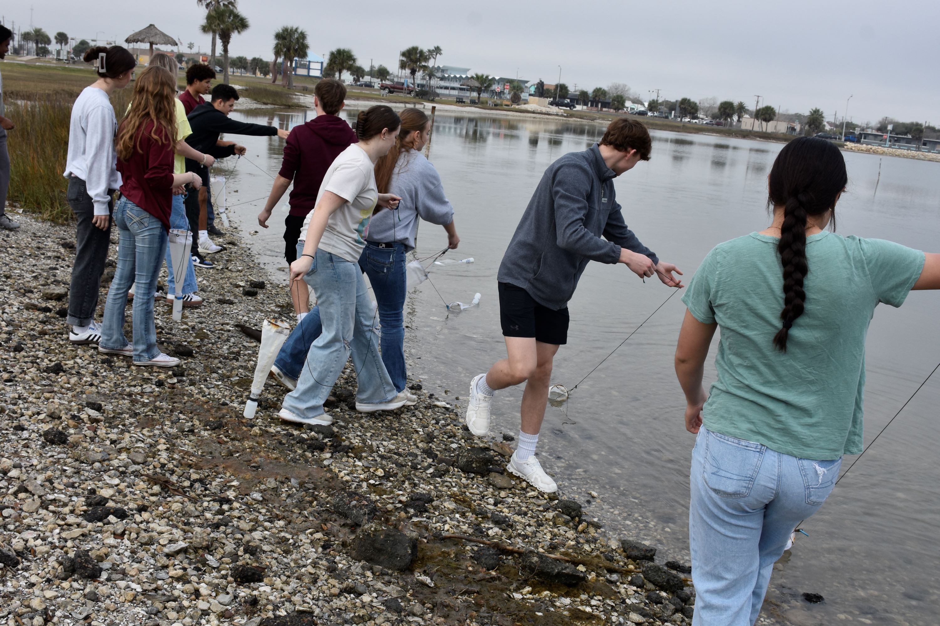High school students take water samples along the shoreline.