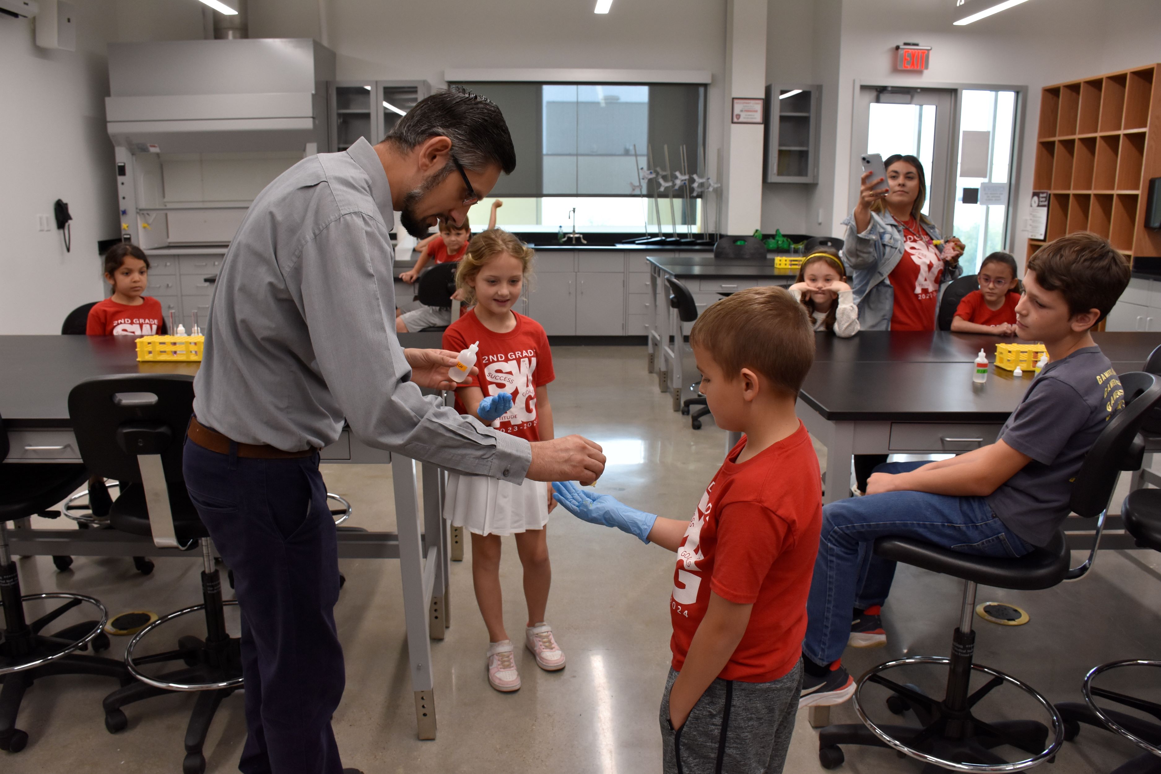 Aleksandr Pikalov puts chemicals in the gloved hands of two children for a chemistry demonstration.