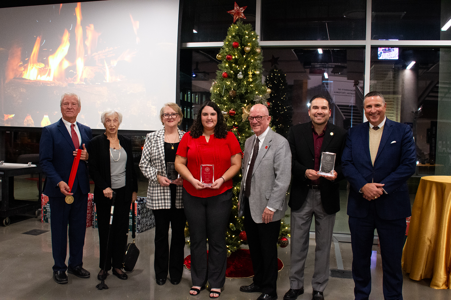 Award winners pose for a photo with awards and a Christmas tree.