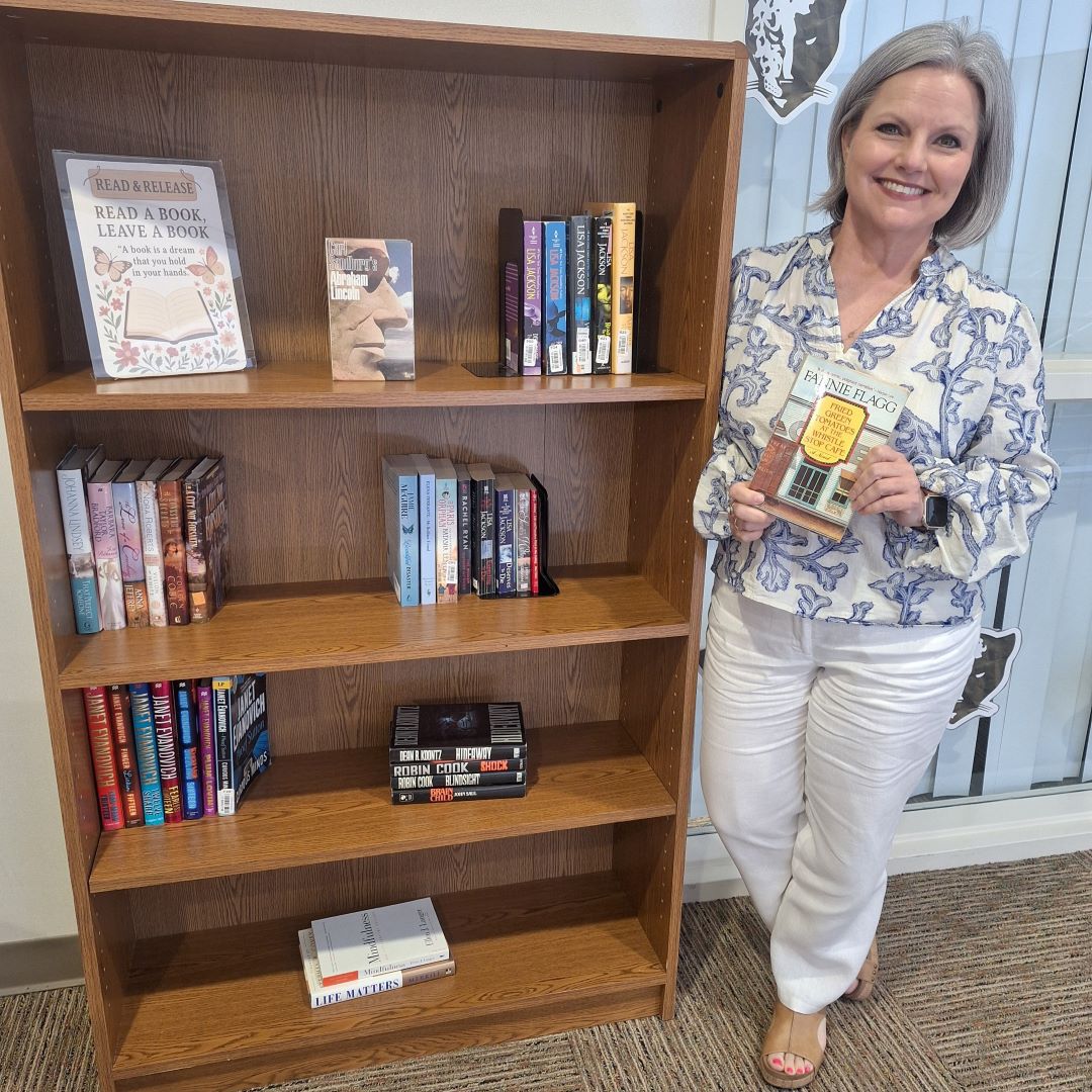 Nancy Gresham stands next to the Lending Library bookshelf.
