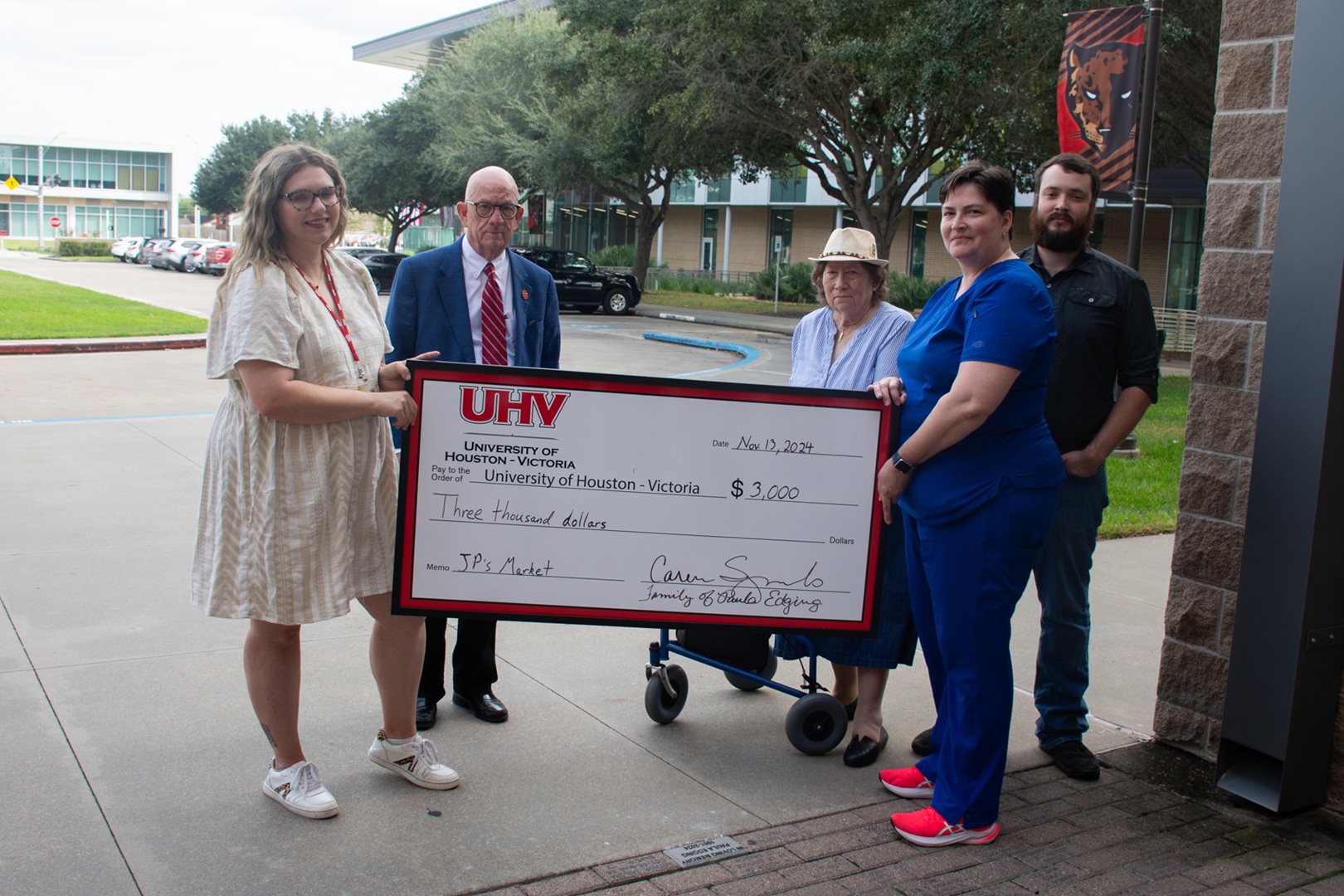 A group of people holding a large ceremonial check from the family of Paula Edging. The check, dated November 13, 2024, is made out to JP's Market for $3,000
