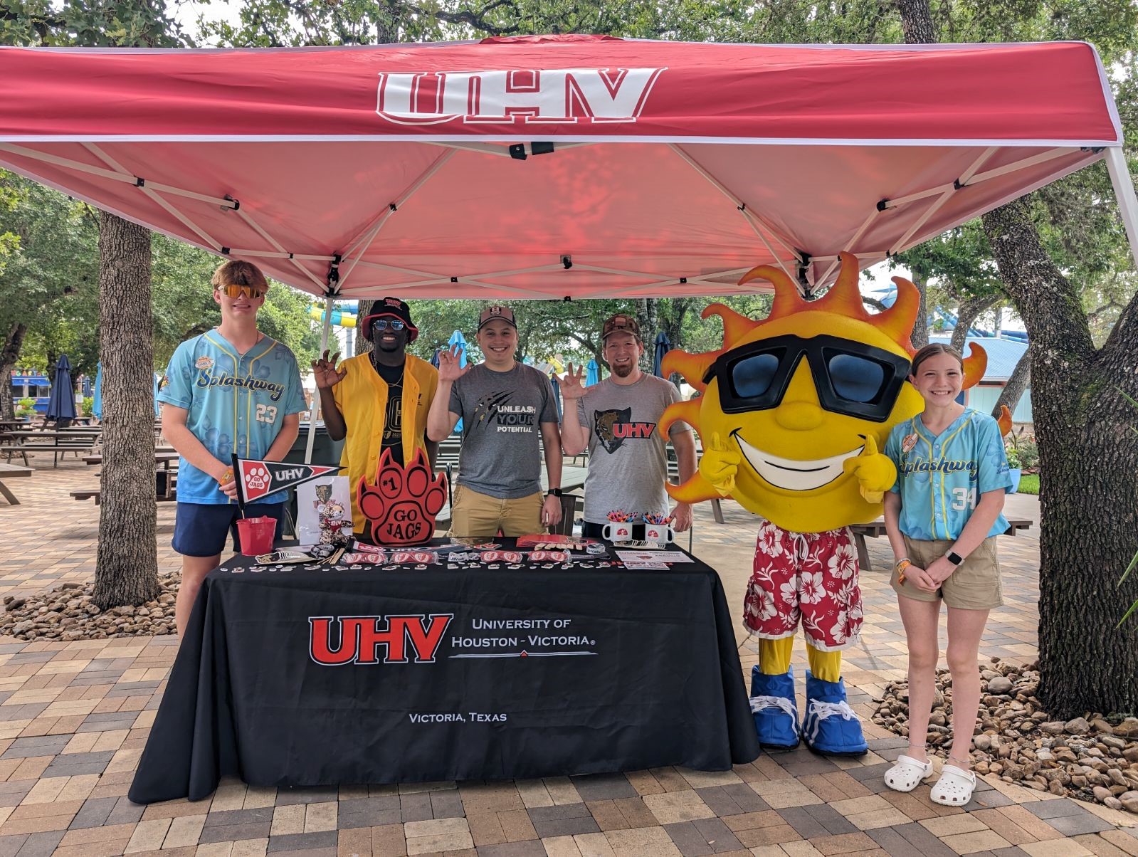 Five people stand under a red UHV tent with a sun mascot.