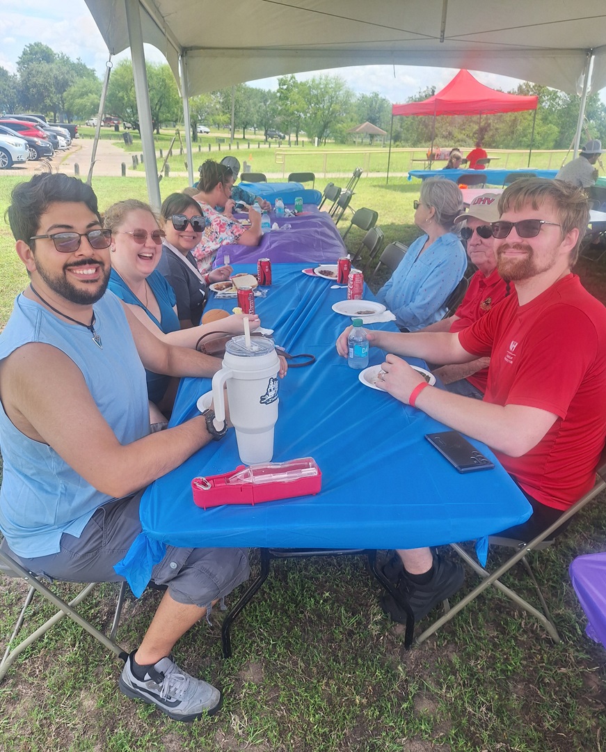 A group of people sit at a table under a tent.