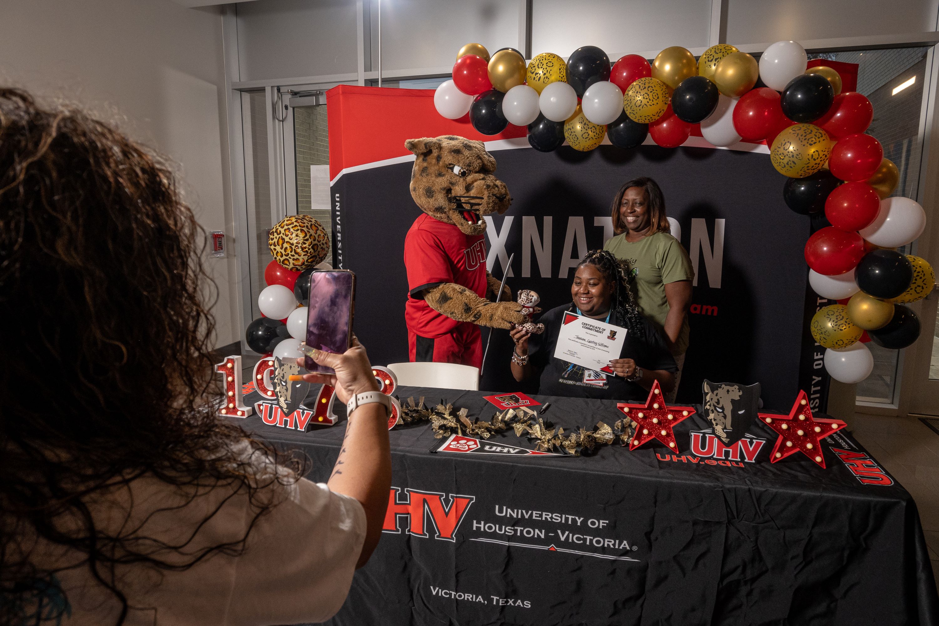 A female student takes a photo with jaX the Jaguar mascot and an older woman